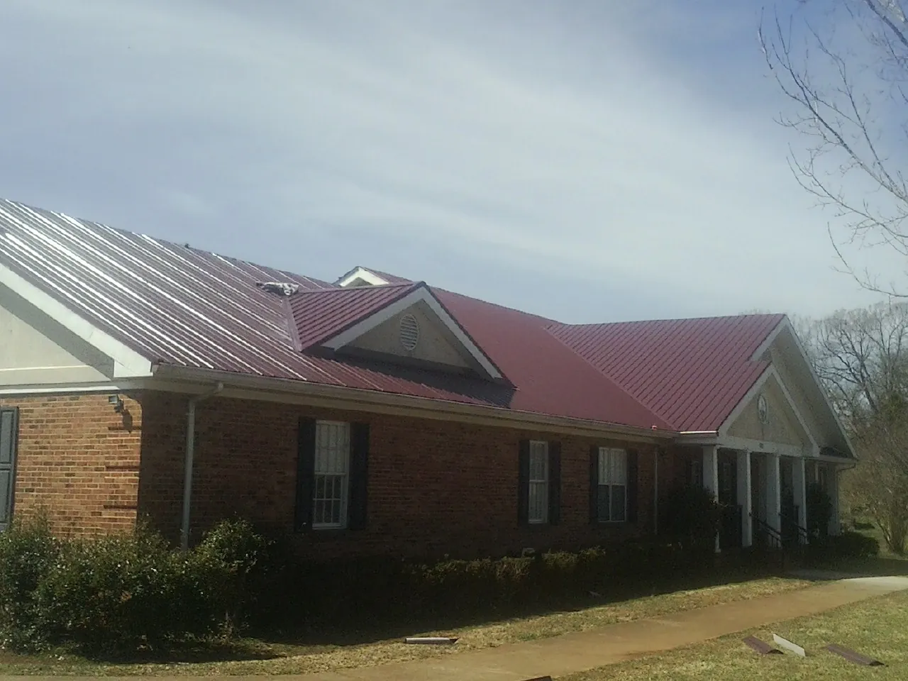 Red metal roof with gabled entries on a long brick building, from a Hail Damage Roof Repair job in Altadena