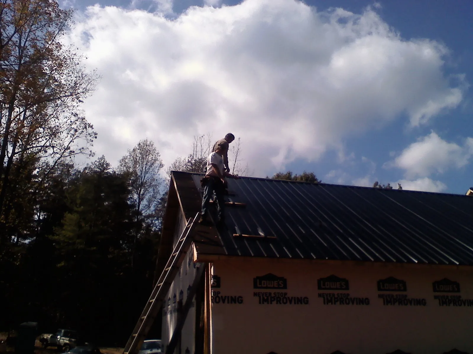 Roofer fastening dark metal panels high against a cloudy sky, from a Roof Inspection job in Altadena